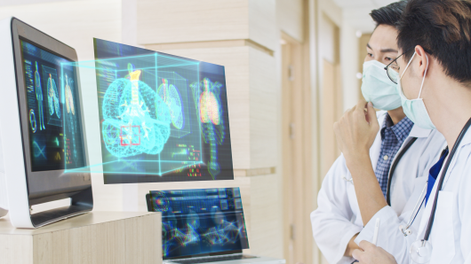 Two masked health care workers looking at AI images on a computer screen