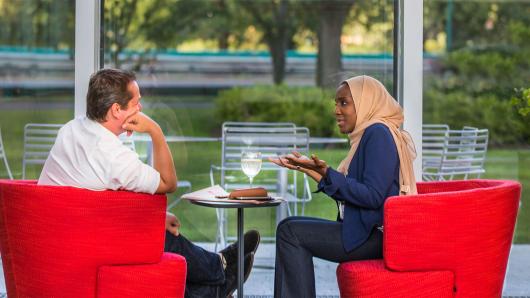 A white male and black female executives in bright red chairs having a conversation