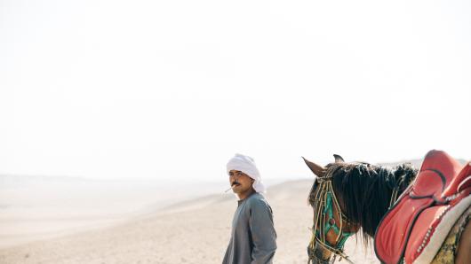 Man walking in the desert with horse.